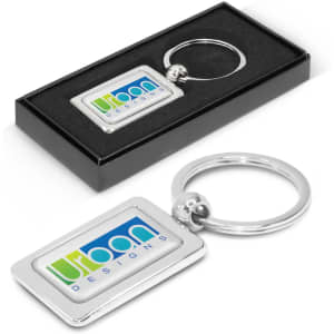 A rectangular metal key ring with a silver finish, presented in a black gift box, featuring a logo.
