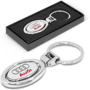 A silver metal key ring with an oval design, presented in a black box, featuring a logo.