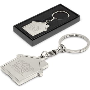 A metal key ring shaped like a house, featuring a logo, presented in a black box. Silver in colour.
