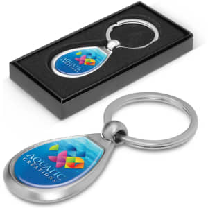 A metal key ring with a teardrop shape, featuring a blue and multicoloured design, presented in a black box.