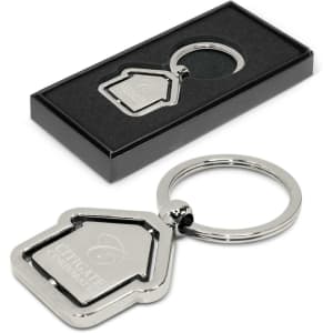 A metal key ring shaped like a house, presented in a black box with a logo on the key ring.