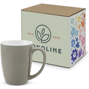 A green coffee mug beside its decorative box, featuring a floral design and branding.