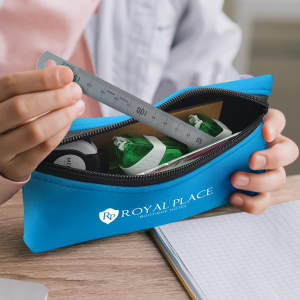 A blue pencil case with a zipper, containing a ruler and green highlighters, held by a person. Features a logo.