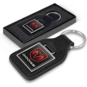 A square black leather key ring with a logo, presented in a black gift box with a grey interior.
