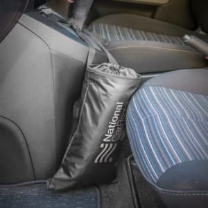 A black Car Tidy bag hanging from a car's centre console, positioned next to a striped seat.