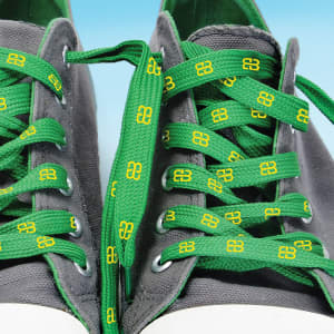 Bright green shoe laces featuring a geometric yellow pattern, threaded through gray sneakers.