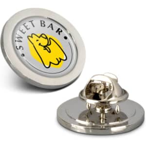 A round, small lapel pin featuring a yellow cartoon character on a silver background, with a logo on the reverse.