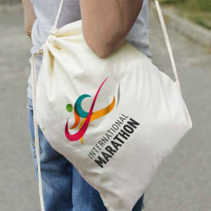 A cream cotton drawstring backpack is being carried, featuring a logo design and a colourful graphic.