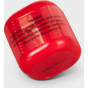 A red lip balm container with a rounded shape, featuring a logo and ingredients listed on the side.