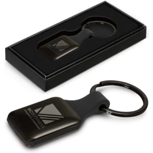 A square black key ring with a shiny surface, presented in a gift box. Features a logo on the key ring.