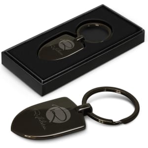 A silver key ring designed as a shovel, presented in a black gift box with a logo.