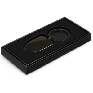 A black gift box containing a green shovel-shaped key ring with a circular attachment.