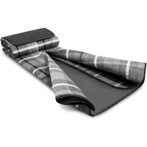 A black and grey checkered picnic blanket rolled partially open, featuring a solid black underside and a branding logo.
