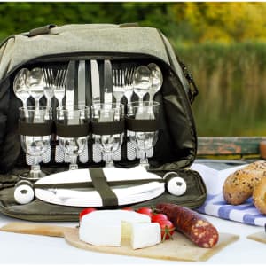 A grey picnic bag with cutlery, glasses, plates, and food items, set against a natural background.