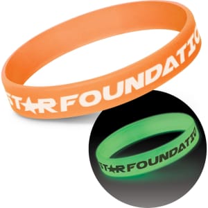 Two silicone wristbands are displayed: one orange and one glowing green in the dark, both featuring a logo.