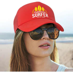 A red trucker cap with a logo, worn by a person with sunglasses and a beach backdrop.
