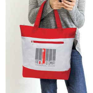 A red and grey tote bag with a zippered pocket and a logo on the front, held by a person using a phone.