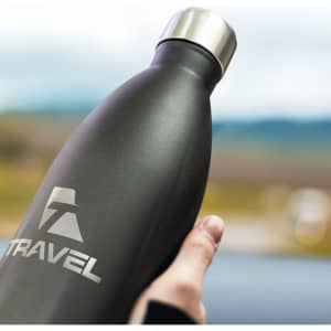 A drink bottle in matte black with a silver lid and a logo, held against a blurred outdoor background.