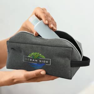 A grey toiletry bag with a zippered closure and a logo, holding a light blue bottle.