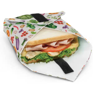 A reusable food wrap featuring a colourful fruit and vegetable pattern, holding a sandwich inside.