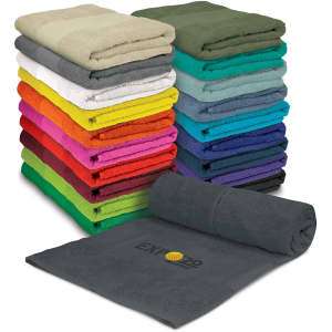 A stack of colourful towels in various shades, including grey, green, and bright hues, with one towel unrolled displaying a logo.