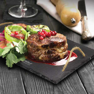 A slate serving board with grilled meat, vegetables, and garnishes, featuring a rustic string handle.