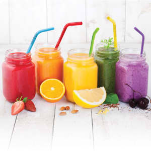 Five jars of brightly coloured drinks with silicone straws in red, blue, green, purple, and yellow, surrounded by fruit.