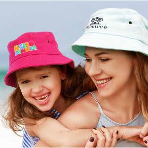A pink bucket hat and a light blue bucket hat worn by a mother and child, both smiling at the beach.