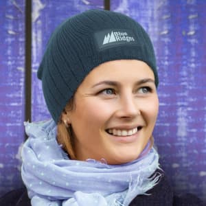 A Nebraska Cable Knit Beanie in a dark teal color featuring a logo patch.