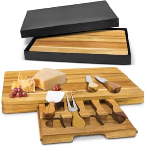 A wooden cheese board with three cheese knives and a black storage box. The board is light brown.