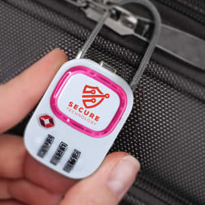 A hand holds a pink and white TSA lock with a logo, designed for securing luggage.