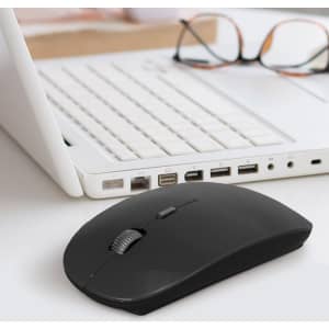 A black travel mouse rests on a desk, next to a white laptop and a pair of glasses. The scene is well-lit and modern.
