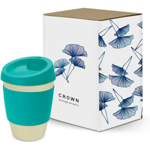A drink bottle with a teal silicone sleeve and a gold base, next to a decorative box featuring leaf designs.