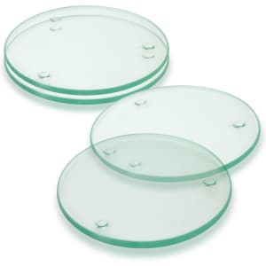 A set of four round glass coasters in a light green hue, featuring raised dots for grip.