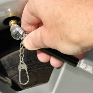 A tyre pressure gauge key ring with a silver and black design, being used to check tyre pressure.