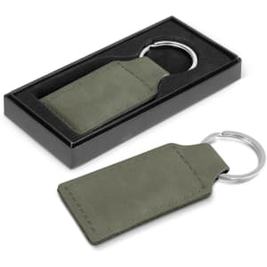 An olive green key ring presented in a black packaging box. It features a metal ring and a rectangular leatherette tag.