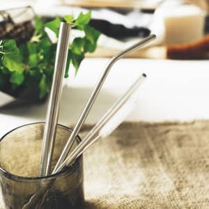 A glass containing three stainless steel straws in silver, featuring a straight, bent, and a cleaning brush.
