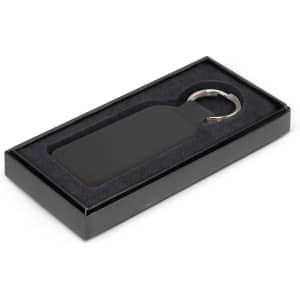 A rectangular black leather key ring displayed in a sleek black box with a soft interior.