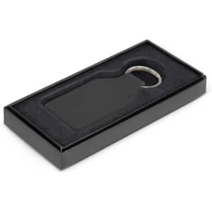 A black square leather key ring presented in an elegant black box with a soft interior.