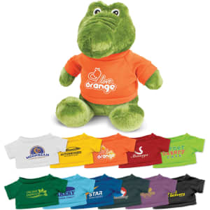 A green crocodile plush toy wearing an orange shirt, surrounded by various small t-shirt designs in multiple colours.