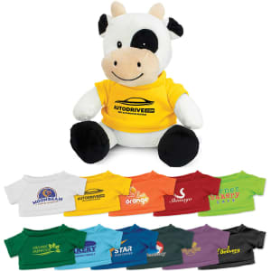 A plush cow toy with a black and white pattern, wearing a bright yellow shirt, accompanied by various colourful shirts.
