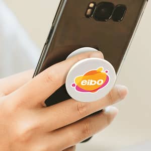 A hand gripping a smartphone with a white circular phone grip featuring a multicoloured logo.