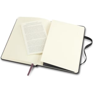 A black Moleskine Classic Hard Cover Notebook opened to reveal blank pages and a small folded leaflet inside.