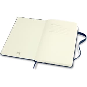 An open Moleskine Classic Hard Cover Notebook in navy blue, featuring blank pages and a ribbon bookmark.
