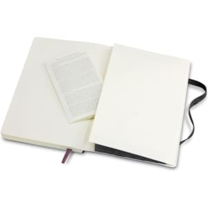 A large, soft cover Moleskine notebook in black with an open page revealing a blank inner page.