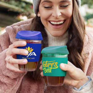 Two women smile while holding drink bottles, one with a blue lid and logo, the other with a green lid and logo, both in a festive setting.