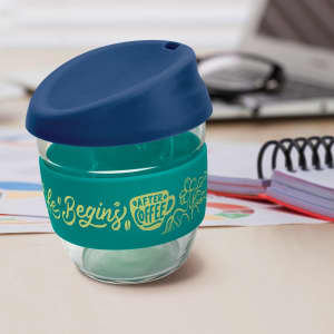 A drink bottle made of clear borosilicate glass, featuring a blue lid and a teal silicone sleeve with designs.