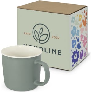 A green coffee mug next to a decorative box featuring floral designs and a logo. The mug has a white interior.