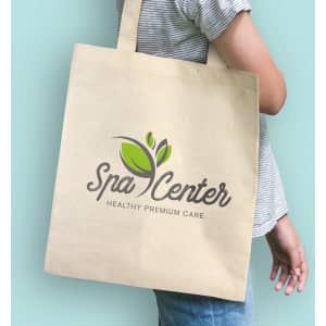Natural beige tote bag featuring a logo with green leaf elements, held by a person against a light blue background.
