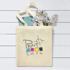 A natural canvas tote bag in cream, featuring a logo and filled with flowers and a blue item.
